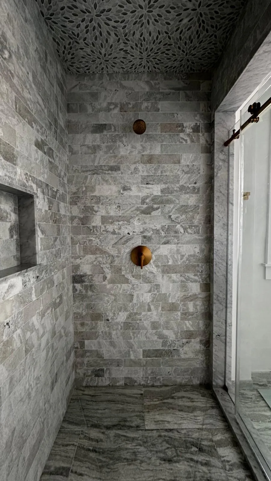 Walk-in shower with gray stone tile, niche and brass fixtures