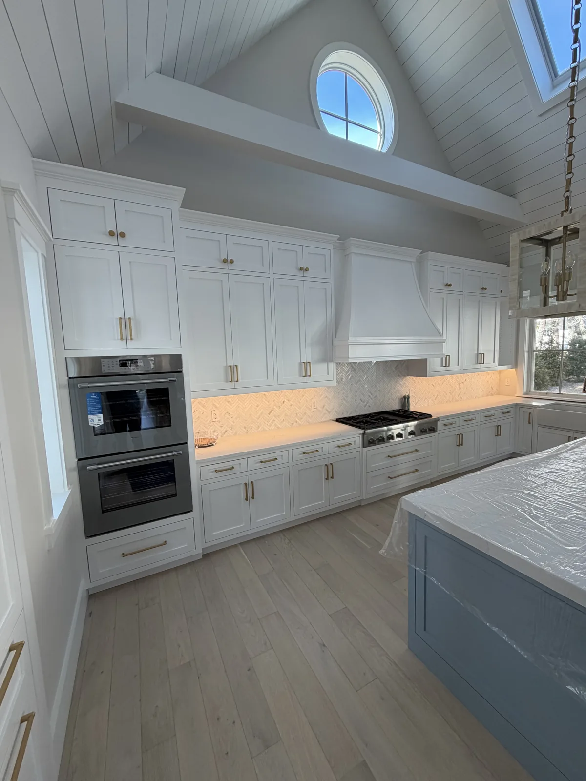 White kitchen with stainless hood, double wall oven and quartz counters