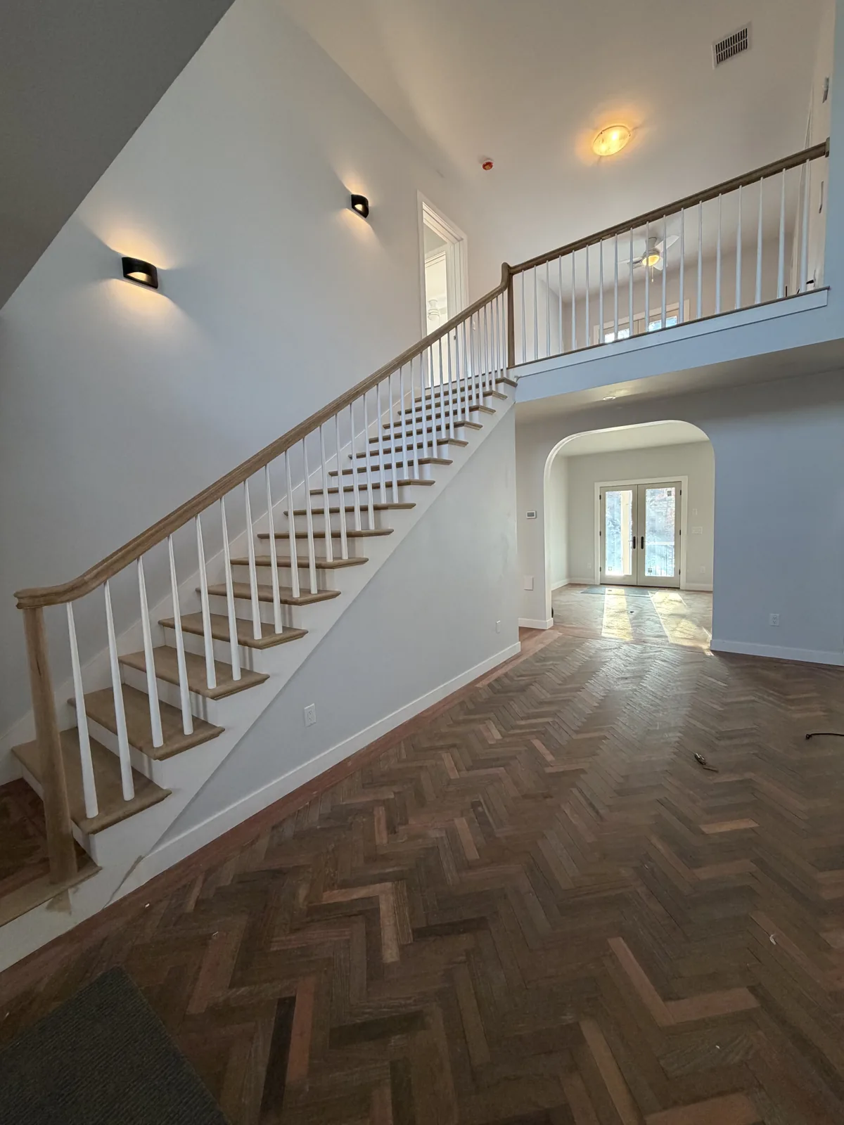 Herringbone wood flooring at the base of a white staircase