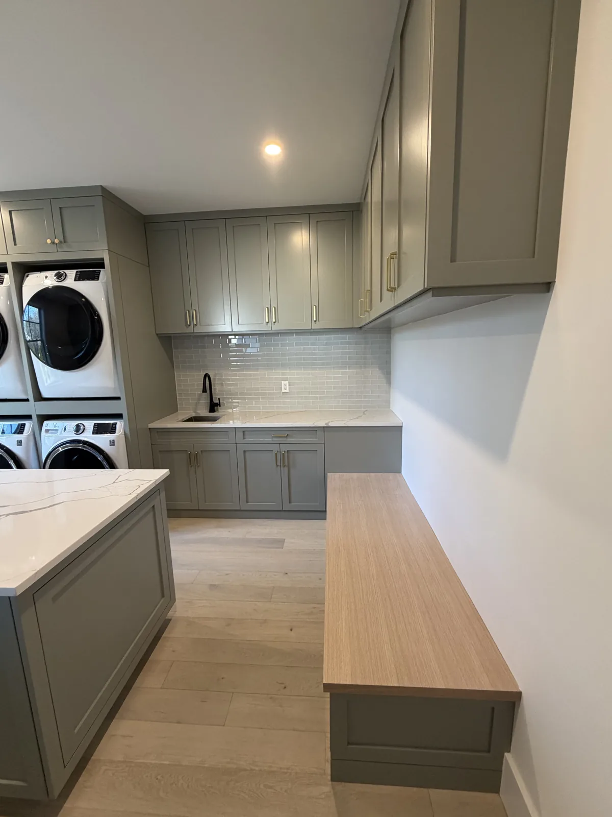 Laundry room with custom cabinetry, bench and stacked machines