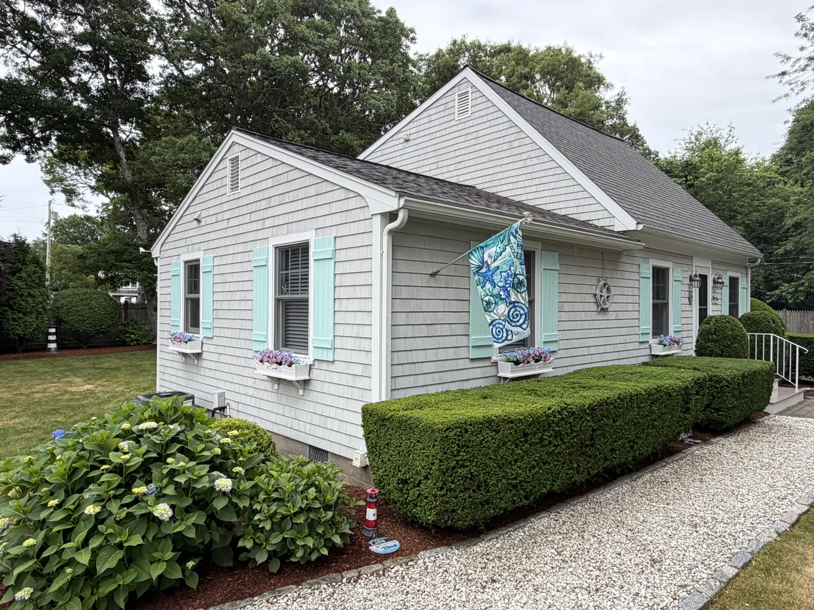 White Cape home with blue shutters and trimmed hedges