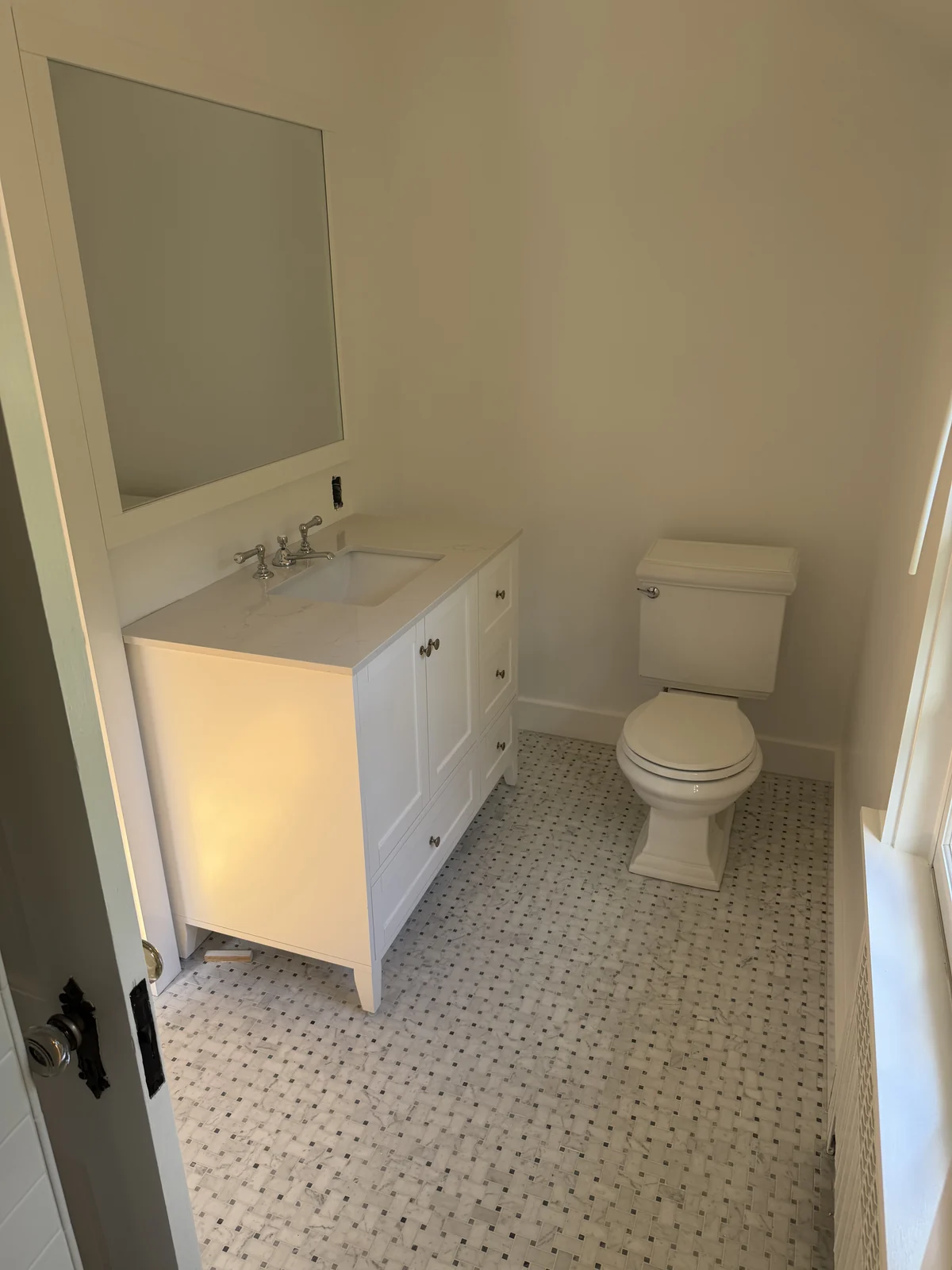 Bathroom with a white vanity, framed mirror and marble basketweave tile floor