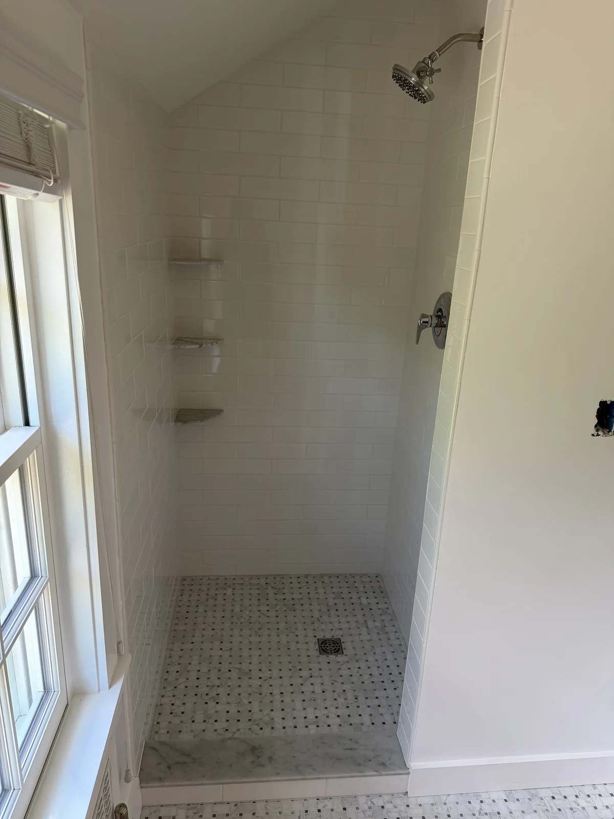 Subway tile shower with corner shelves and a marble mosaic shower floor